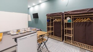 Una stanza piccola e luminosa, con un letto, una scrivania con un computer e un armadio pieno di vestiti.