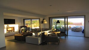 A modern living room with a sofa, armchairs, and a coffee table. There is a TV mounted on the wall, a large window, and a view of the outdoors. - Villa Veintidos Large Luxury Villa Sleeps 12 (El Portet, Moraira)
