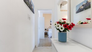 Un pasillo con piso de baldosas, un jarrón azul con flores y una cama al fondo.