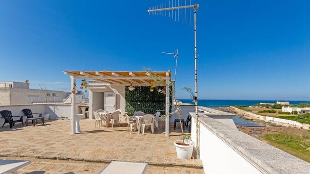 Una terraza en la azotea con mobiliario exterior, una pérgola y vistas al mar.