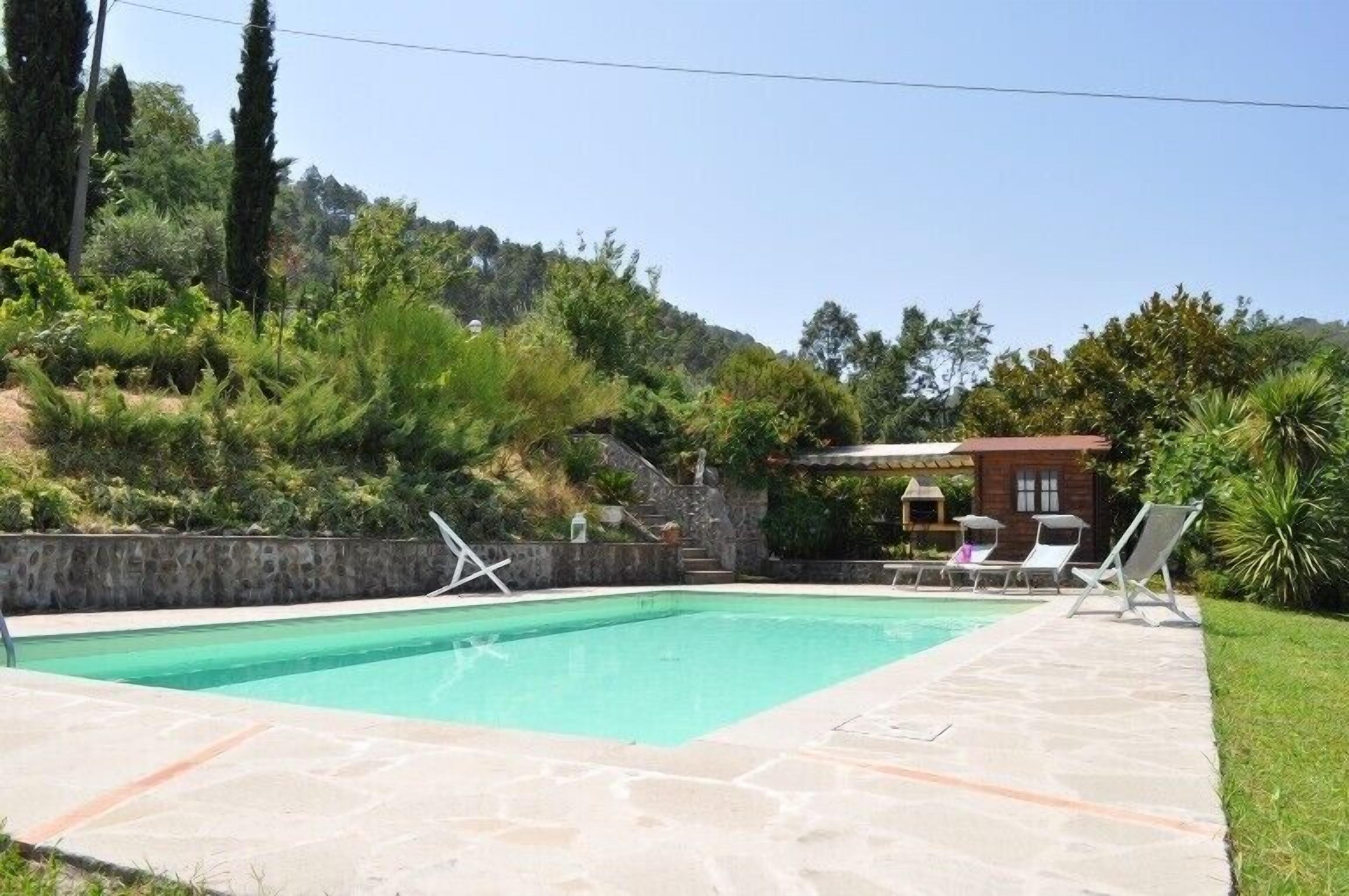 Ein Pool mit Liegestühlen, einer Steinmauer und einem Gebäude im Hintergrund.