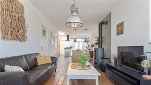 En moderne stue med en lædersofa, et hvidt sofabord, et fladskærms-tv og et køkken i baggrunden.