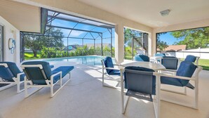 Área da piscina com espreguiçadeiras e mesa, janelas amplas com vista para a piscina e vegetação.