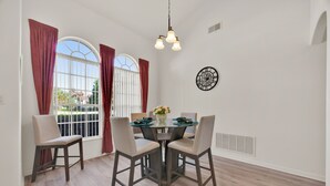 Uma área de refeições com uma mesa redonda, quatro cadeiras, um vaso com flores e um relógio de parede.