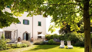 A well-maintained garden with a white building, a covered patio, and two lounge chairs.