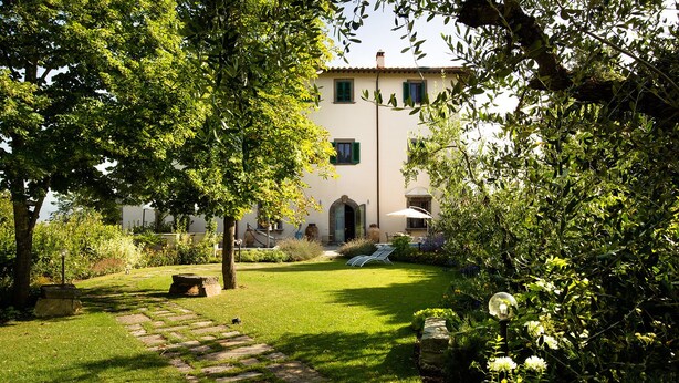 A garden with a stone pathway leading to a building with a white facade and green shutters.