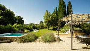 A poolside area with a pergola, outdoor seating, and a view of the surrounding garden.