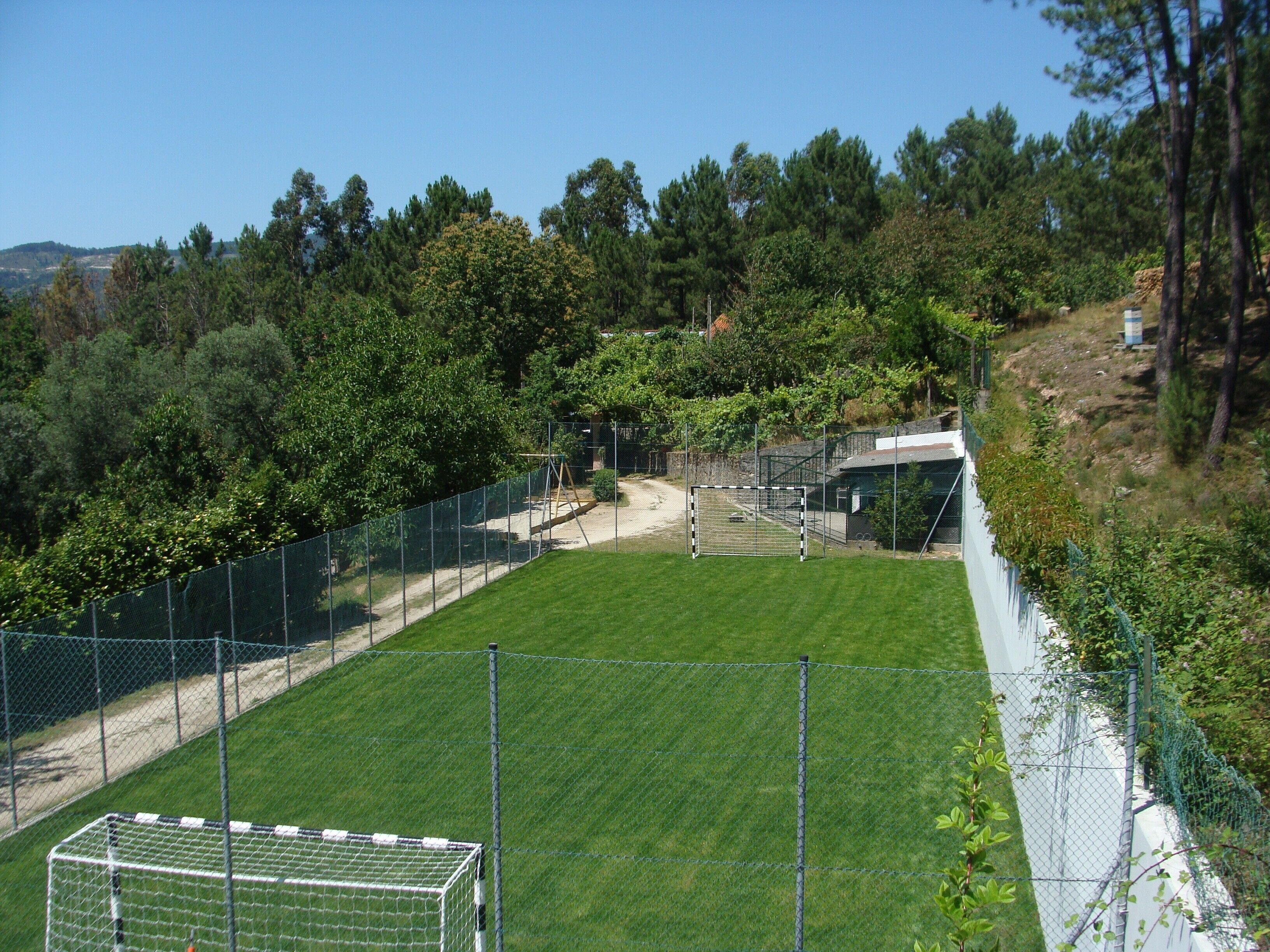A fenced soccer field with a goalpost, surrounded by trees and a hilly landscape.