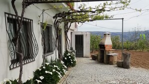 Un camino adoquinado que conduce a un edificio con una pérgola cubierta de hiedra, un horno de ladrillo y vistas al campo.