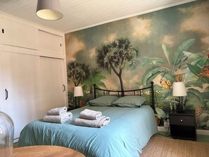 A bedroom with a bed, two bedside lamps, a nightstand, and a wall mural of tropical foliage. - Large family home with private pool (Dévillac)