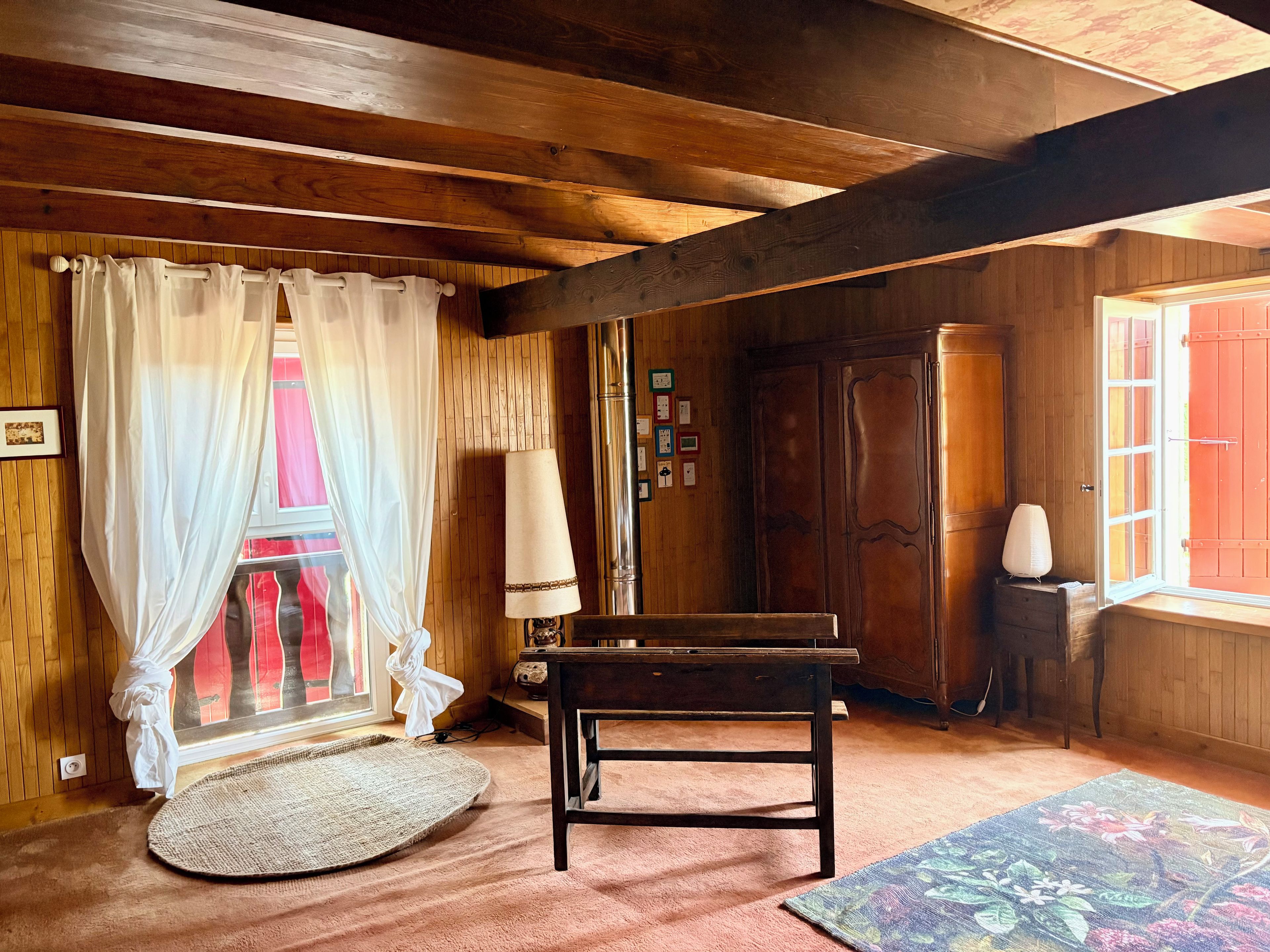 A room with wooden beams, a piano, a lamp, and a window with curtains.