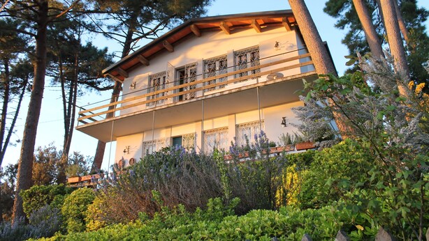 Ein zweistöckiges Gebäude mit Balkon, umgeben von Bäumen und Sträuchern.
