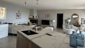 Una cocina moderna con encimera de mármol, pileta integrada y comedor con mesa y sillas blancas.