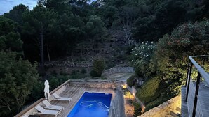 Una terraza de madera con piscina, sillas de descanso y un muro de piedra.