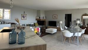 Una sala de estar moderna con chimenea, un comedor con sillas blancas y una cocina con encimera de mármol.