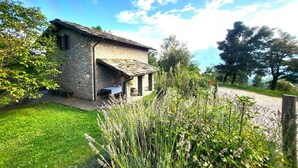 A stone house with a sloped roof, a small porch, and a grassy yard with wildflowers. - Fabulous Spectacularly Located Romantic Cottage With Private Infinity Pool (Carregine)