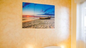 Een kamer met twee bedden, een schilderij van een zonsondergang boven de zee aan de muur, en een raam met gordijnen.