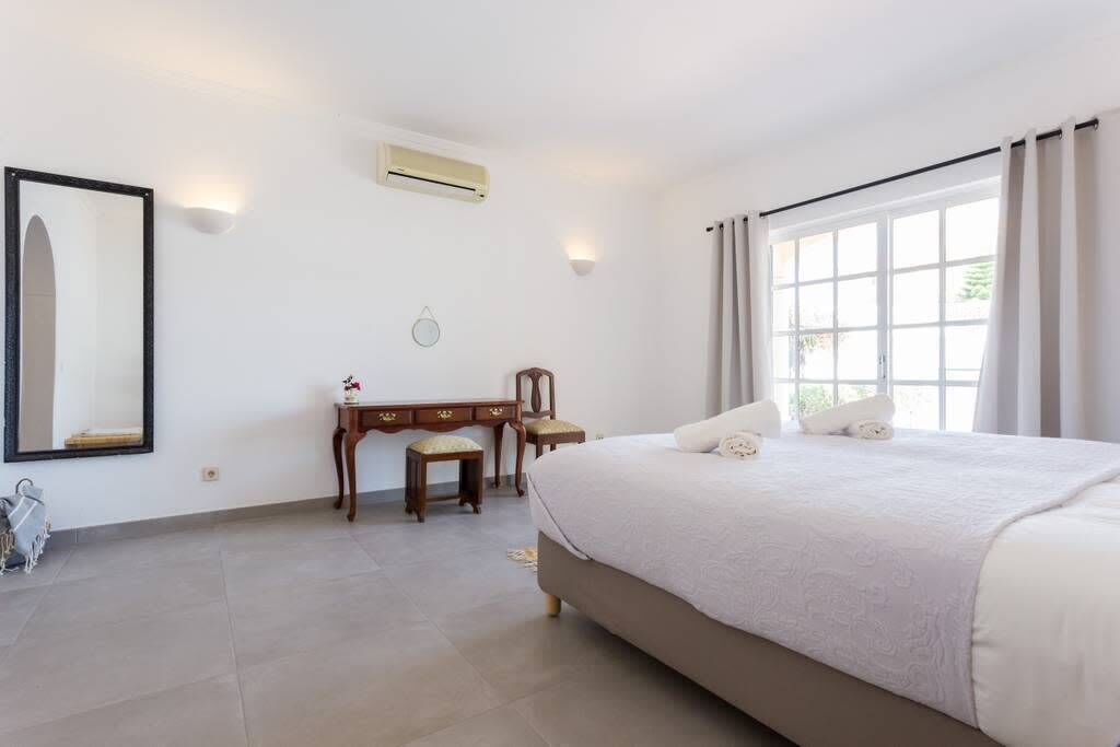 A bedroom with a large bed, a desk, a chair, and a mirror.