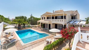 A two-story house with a swimming pool, outdoor seating, and a garden.
