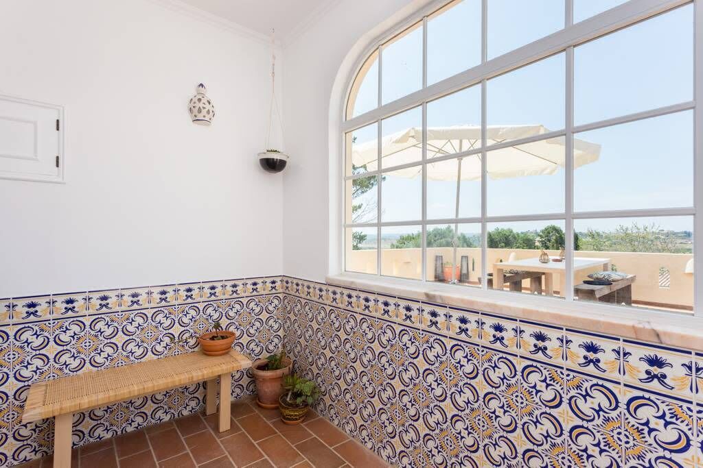 Une pièce d’angle avec un banc, des plantes en pot et une vue sur l’extérieur grâce à une grande fenêtre.