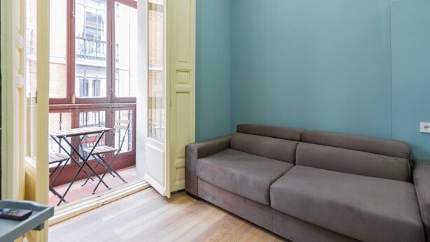 A room with a sofa, a table, and a balcony with a view of buildings. - BED AND BREAKFAST ONLY HUERTAS-2 (Madrid)
