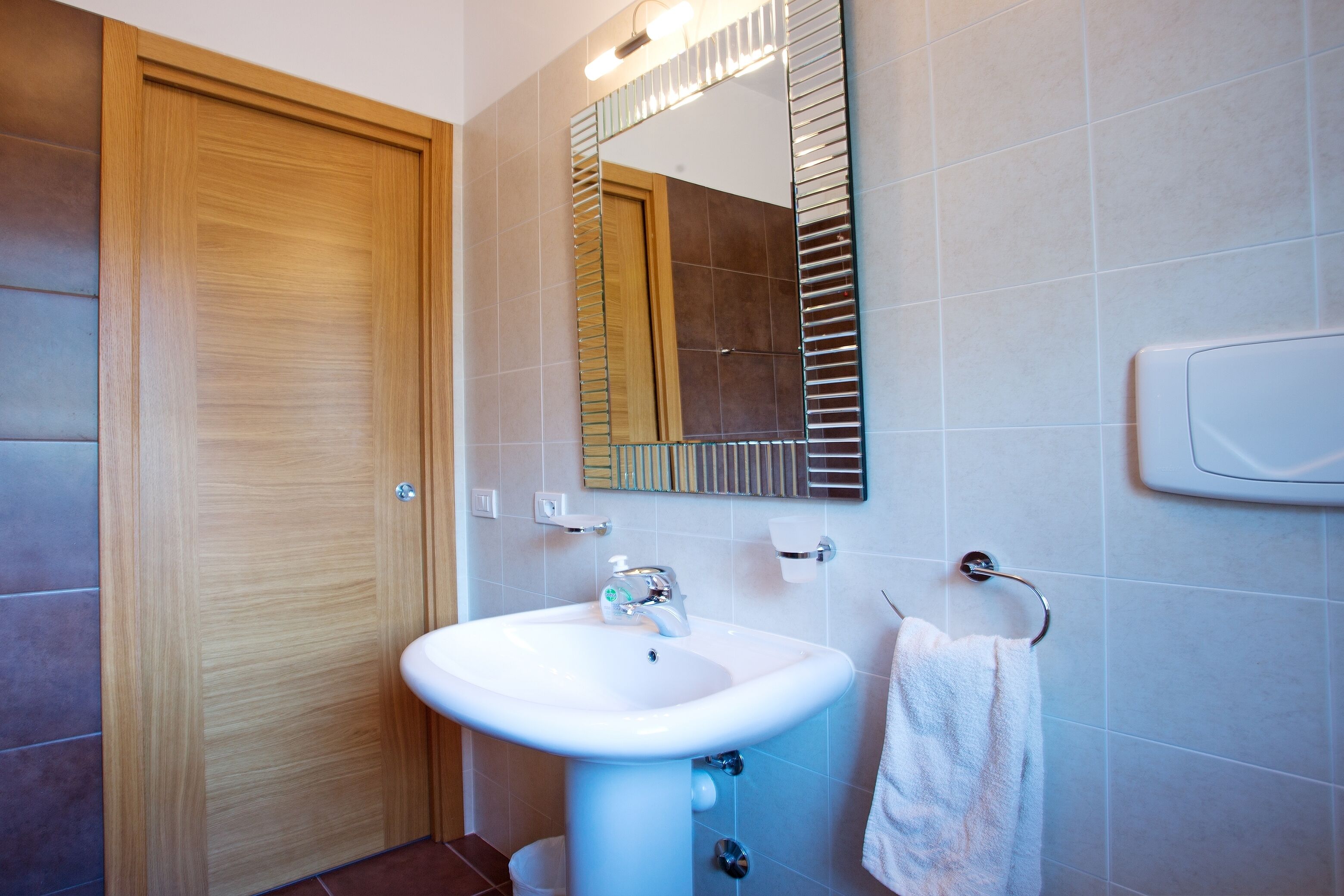 A modern bathroom with a wooden door, a white sink, a mirror, and a towel rack.