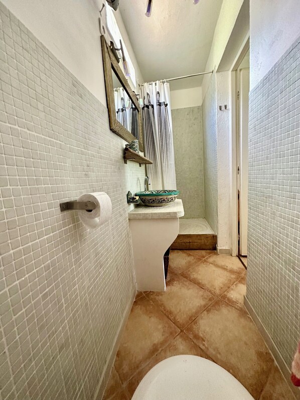 A bathroom with a toilet, a sink with a decorative basin, a mirror, and a towel rack.