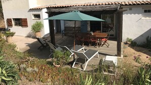 Een terras met een tafel, stoelen, een groene parasol en potplanten.
