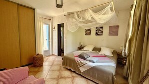 Een slaapkamer met een bed, een nachtkastje, een lamp, een hanglamp, een rieten mand en een gestreepte bank.