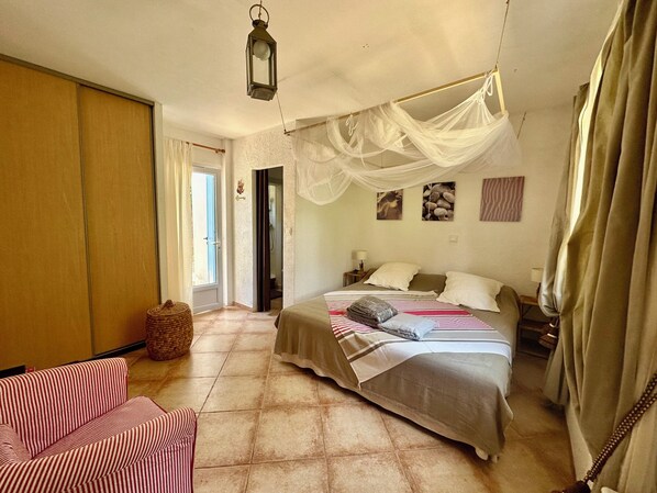 A bedroom with a bed, a nightstand, a lamp, a hanging lantern, a wicker basket, and a striped sofa.