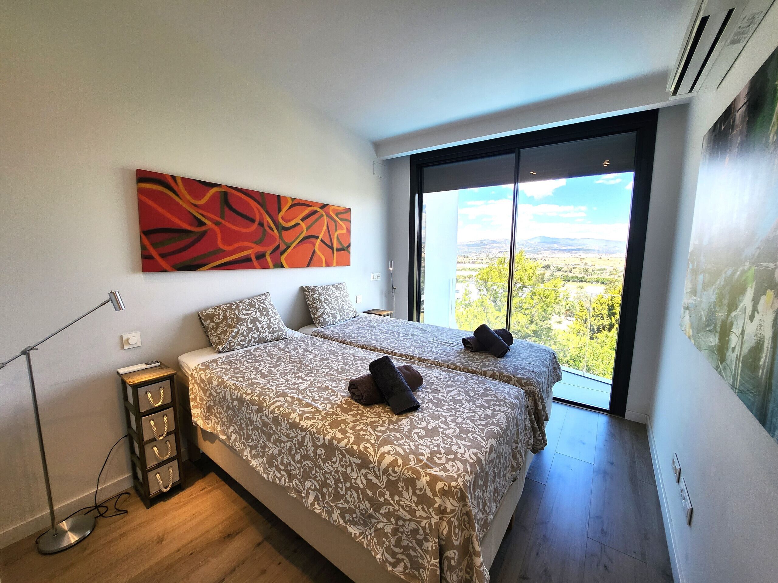 Ein modernes Schlafzimmer mit zwei Betten, einem großen Fenster mit Blick auf die Stadt, einer Stehlampe und einem Bild an der Wand.