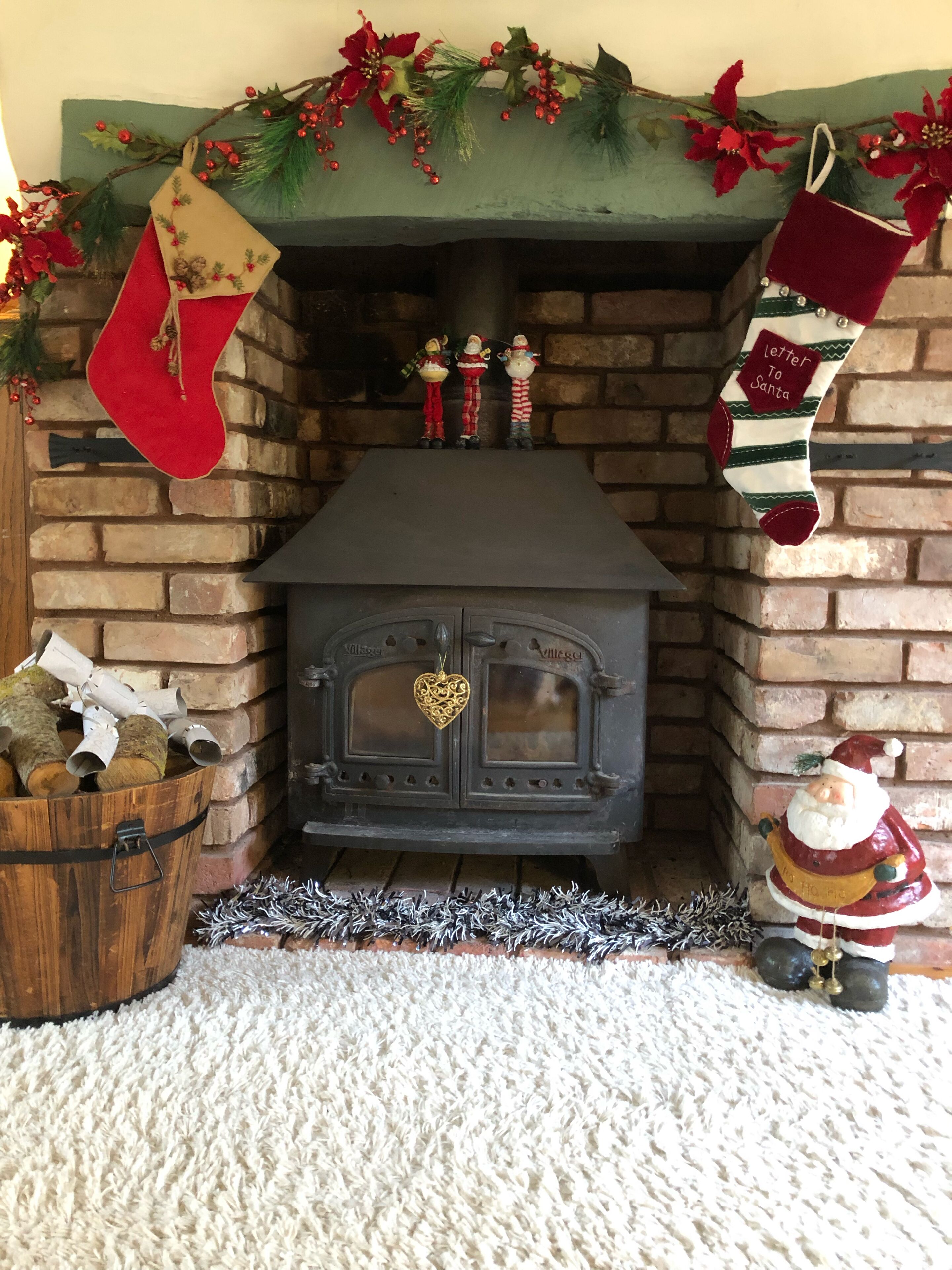 Une cheminée au décor rustique en briques, agrémentée de décorations de Noël et de bas de cheminée.