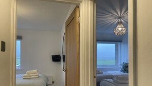 A hotel room with a view of the sea, a chandelier, and a bed with a white comforter. - Westward 14, Polzeath, North Cornwall  (Polzeath)