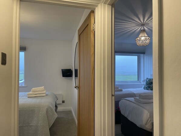 A hotel room with a view of the sea, a chandelier, and a bed with a white comforter. - Westward 14, Polzeath, North Cornwall (Polzeath)