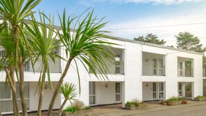 A two-story white building with balconies, surrounded by palm trees and potted plants. - Westward 14, Polzeath, North Cornwall  (Polzeath)