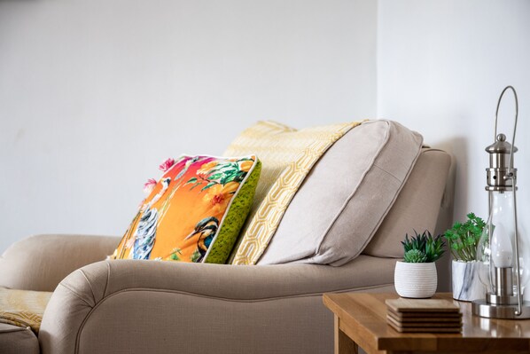 Ein beiges Sofa mit bunten Kissen, ein kleiner weißer Topf mit einer Sukkulente und eine Metalllampe auf einem Holznachttisch.
