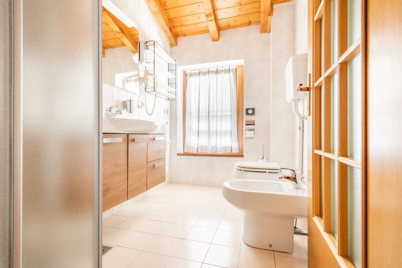 Ein modernes Badezimmer mit Holzboden, einem großen Fenster mit Vorhängen, einem Waschbecken und einem Bidet.