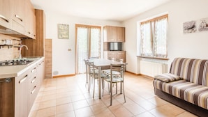 A modern kitchen with wooden cabinets, a dining table with chairs, a sofa, and a radiator.