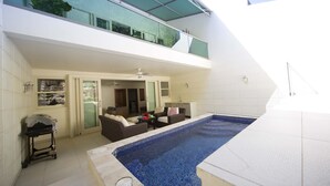 A modern outdoor pool area with a glass balustrade, a seating area with sofas, and a grill. - Stunning Hillside Villa, Limegrove St James (Holetown)
