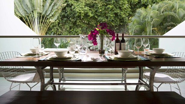 A dining table set for two with white plates, glasses, and a vase of flowers. - Stunning Hillside Villa, Limegrove St James (Holetown)