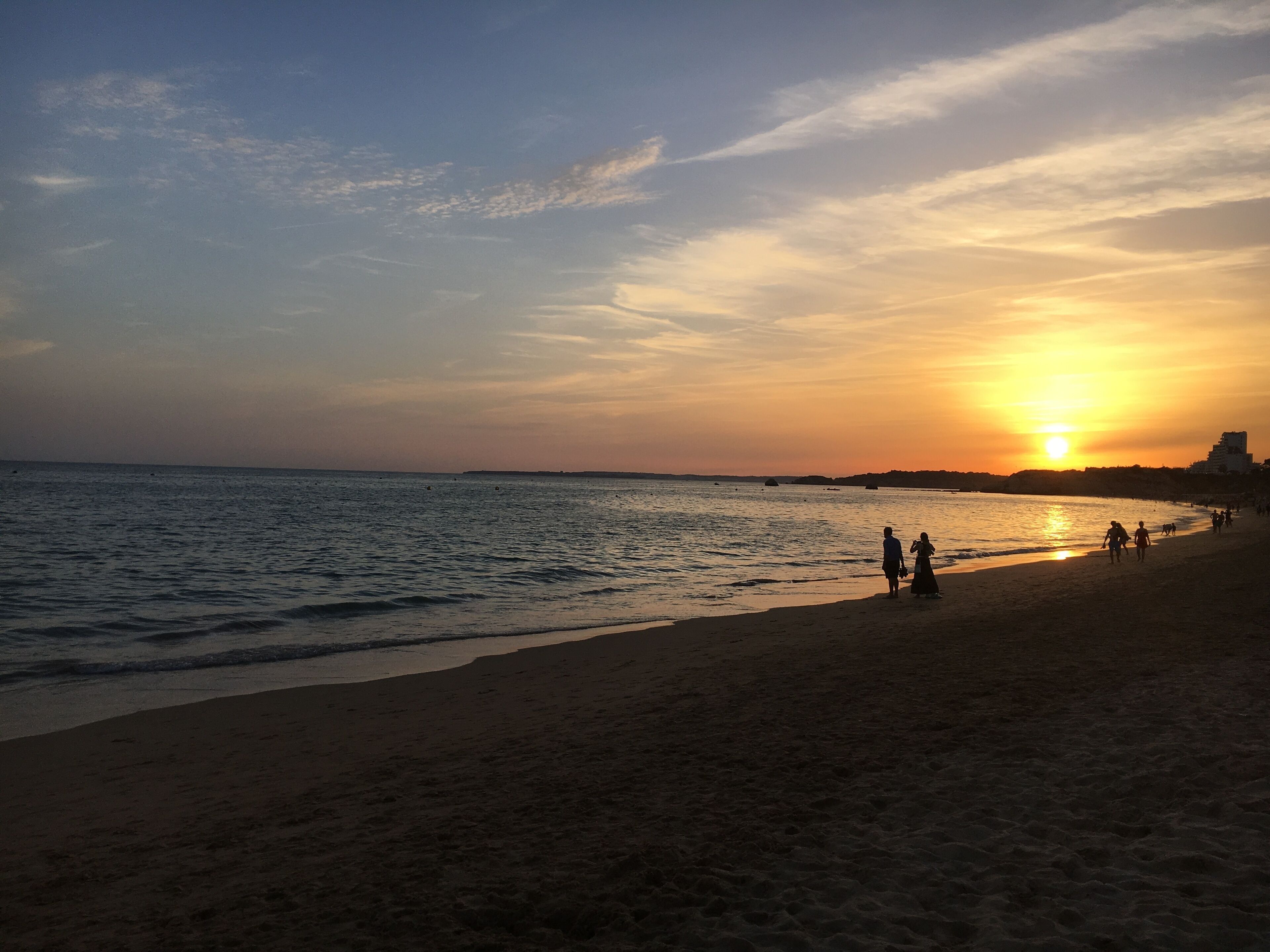 A beach at sunset with calm waters and a clear sky.