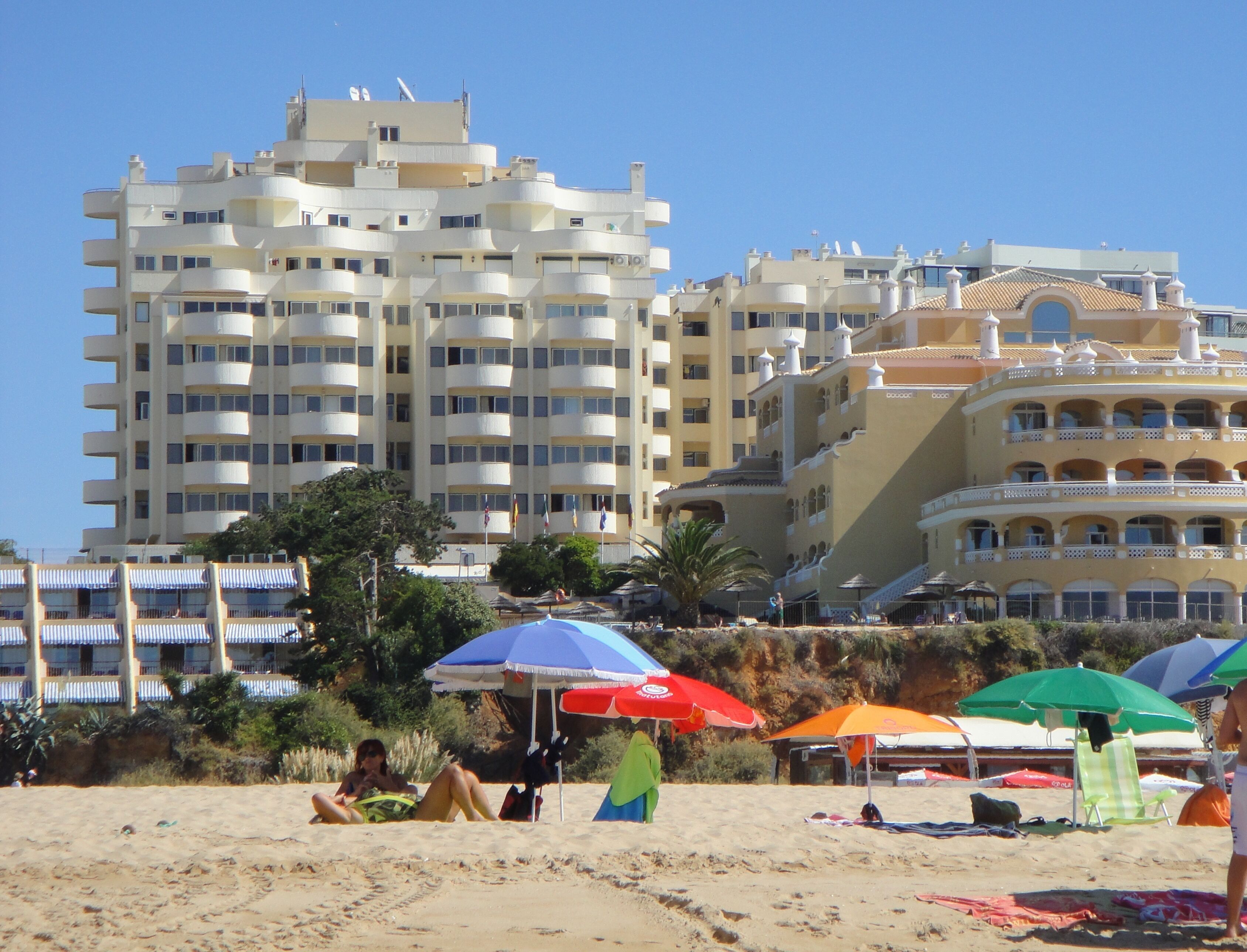 Une plage avec un grand hôtel en arrière-plan, doté de nombreux balcons et présentant un style architectural particulier.