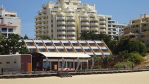 Un hotel frente a la playa con diseño moderno, que cuenta con un área de estar cubierta al aire libre y varios balcones.