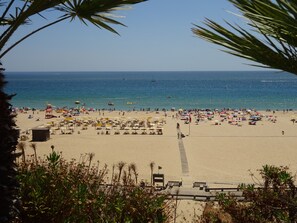 Una playa con numerosos sombrillas y tumbonas, un cielo azul despejado y el océano al fondo.
