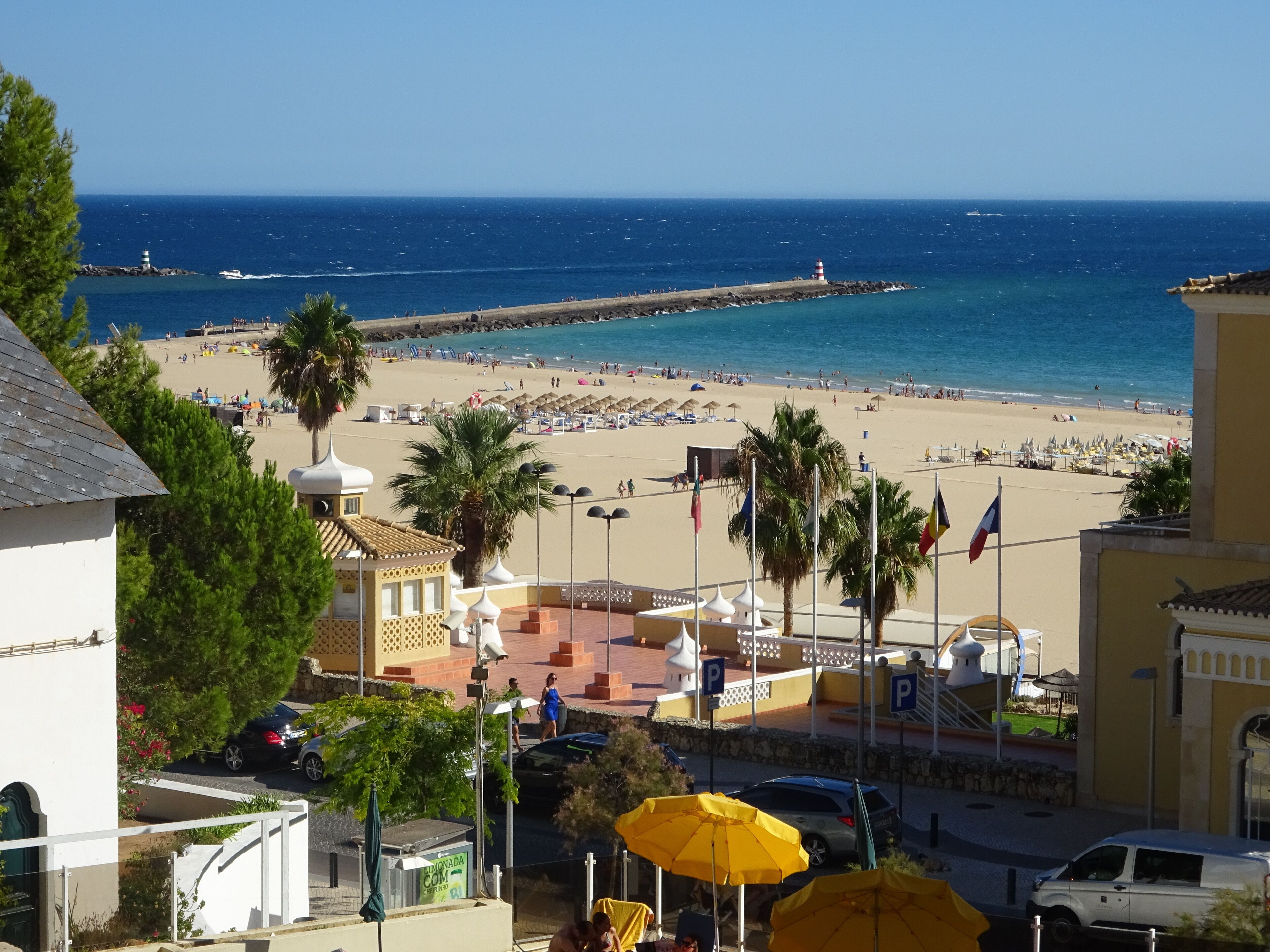 A coastal view with a beach, palm trees, and a lighthouse in the distance.