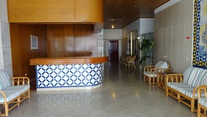 Una zona de recepción con mostrador de madera, baldosas con diseño, muebles de mimbre y suelo de baldosas.