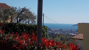 A view from a covered balcony overlooking a coastal town with a bridge in the distance. - APARTMENT IN VILLA WITH GARDEN AND SEA VIEW (La Spezia)