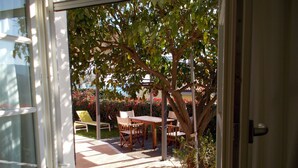 A view through a window of a patio area with a table and chairs, surrounded by greenery and a small tree. - APARTMENT IN VILLA WITH GARDEN AND SEA VIEW (La Spezia)