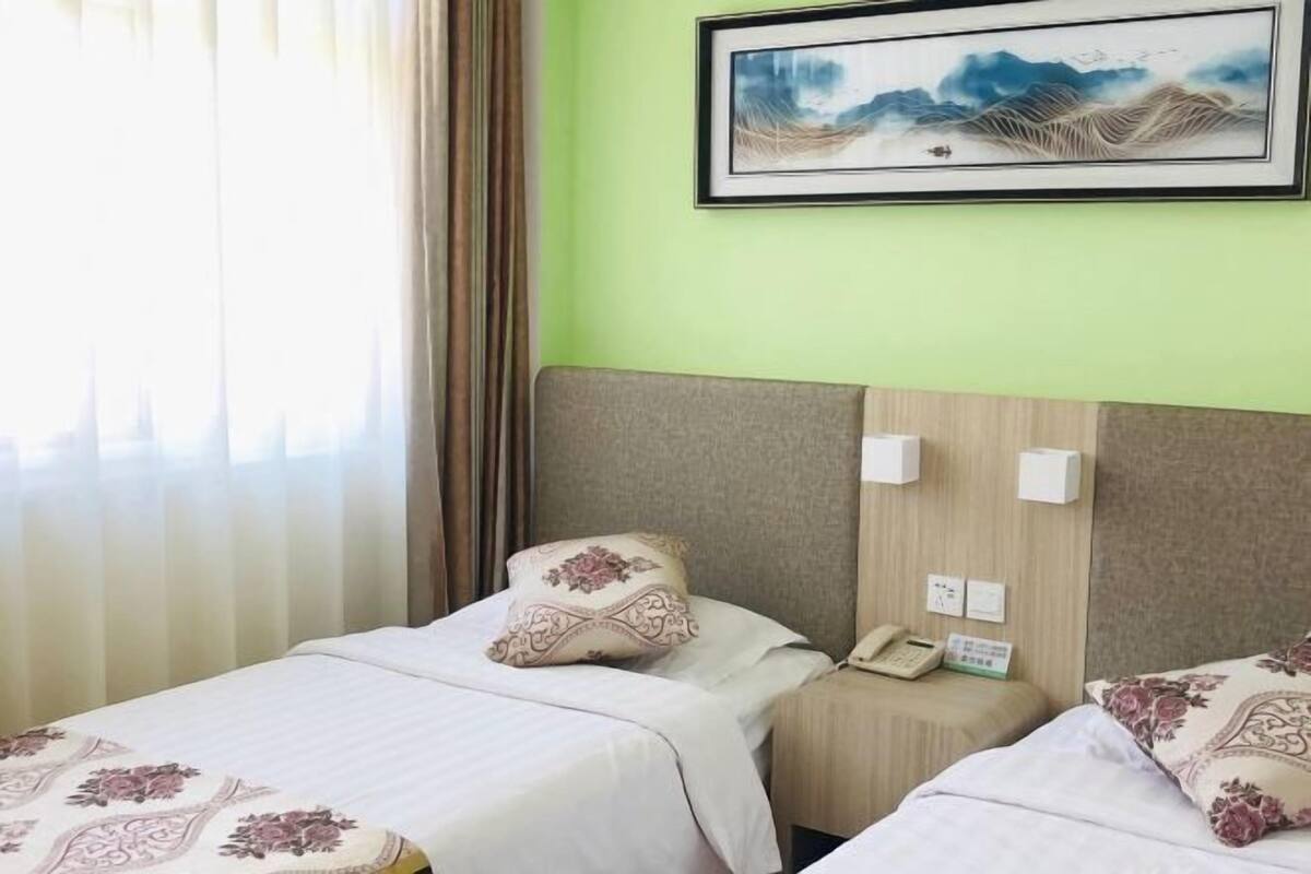 A hotel room with two beds, a painting on the wall, and a window with curtains.