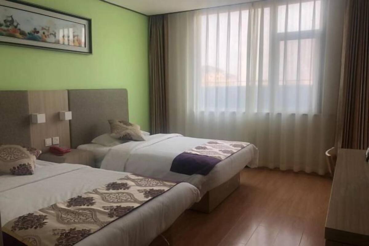 A hotel room with two beds, a painting on the wall, and a window with curtains.